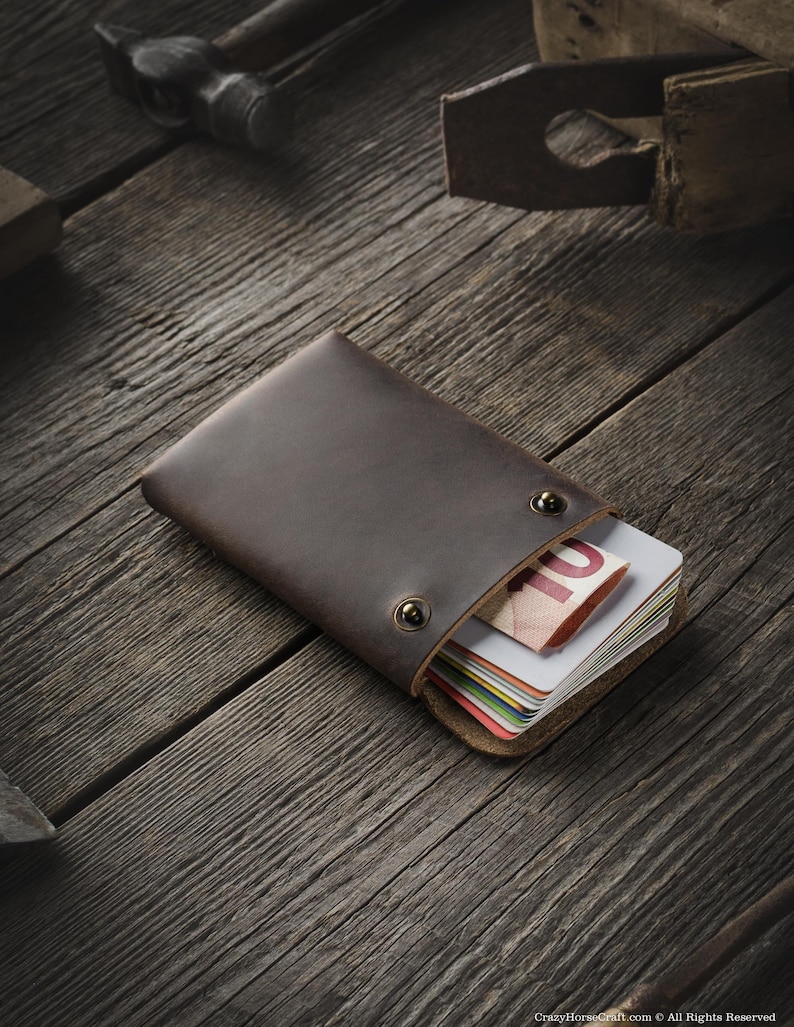 May include: A brown leather wallet with a stack of credit cards and a ten euro bill inside. The wallet is on a wooden surface.