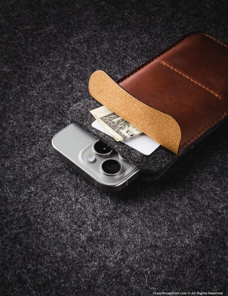 May include: A brown leather phone case with a flap that folds over the top of the phone. The case is lined with a tan fabric and has a pocket for a credit card or cash. A white smartphone with a black camera lens is inside the case.