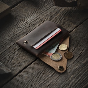 May include: A brown leather wallet with a flap closure, open to reveal cash and coins. The wallet has a snap closure and a single button on the flap.