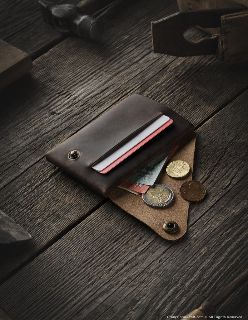 May include: A brown leather wallet with a flap closure, open to reveal cash and coins. The wallet has a snap closure and a single button on the flap.