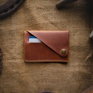 May include: A brown leather wallet with a flap closure and a horseshoe-shaped button. The wallet is on a burlap background.