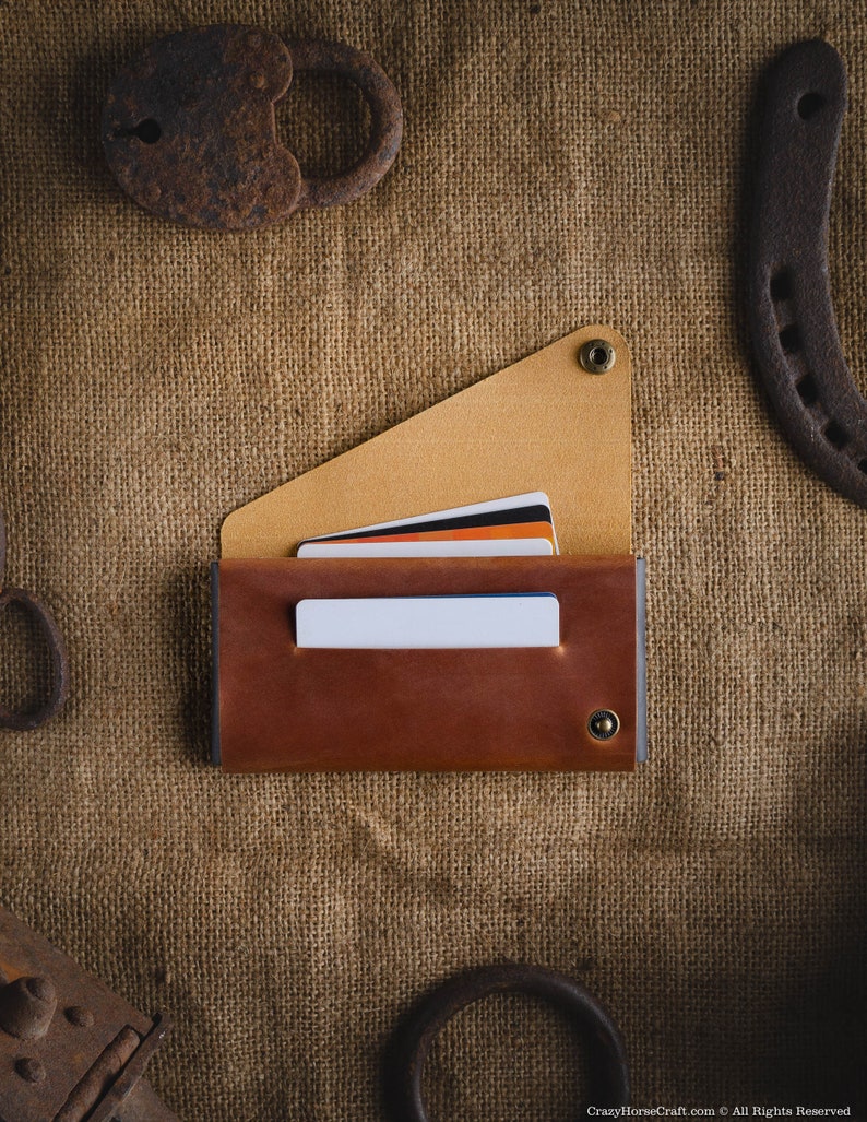 May include: A brown leather wallet with a flap and a snap closure. The wallet has a beige interior and is holding several credit cards. The wallet is lying on a burlap surface.