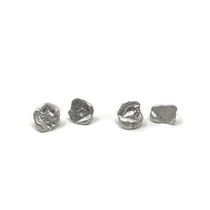 May include: Four silver earrings with a textured, irregular shape. The earrings are small and have a modern, minimalist design.