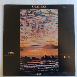 Puede incluir: Una portada de álbum de vinilo negro con una puesta de sol sobre el océano. El álbum se titula "Time and Tide" de Split Enz.