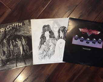 Puede incluir: Tres discos de vinilo de la banda Aerosmith. El primer disco se titula "Toys in the Attic", el segundo se titula "Draw the Line" y el tercero se titula "Rocks".