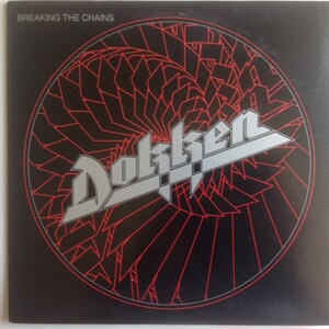 Op de afbeelding: Een zwarte vinylplaat met een zilveren en rood ontwerp. De plaat heeft de bandnaam "Dokken" en de albumtitel "Breaking the Chains".
