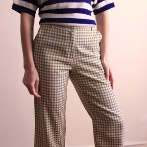 Pu&ograve; includere: Un top a maniche corte con righe orizzontali blu navy e bianche &egrave; abbinato a pantaloni a quadri. I pantaloni hanno un motivo a quadri beige e marrone. L'outfit &egrave; in stile vintage.
