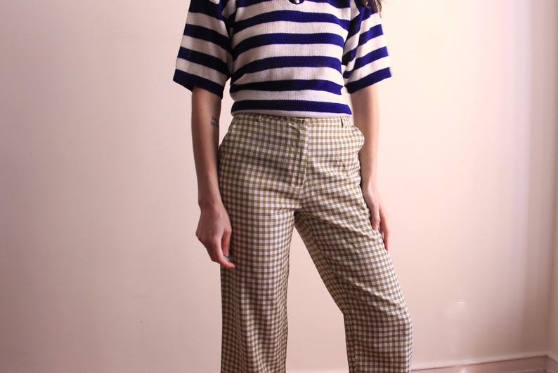 Pu&ograve; includere: Un top a maniche corte con righe orizzontali blu navy e bianche &egrave; abbinato a pantaloni a quadri. I pantaloni hanno un motivo a quadri beige e marrone. L'outfit &egrave; in stile vintage.