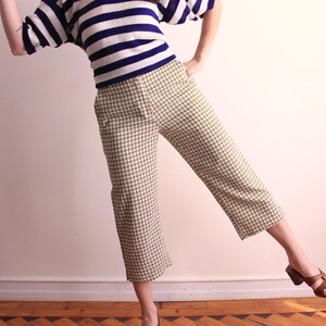 Pu&ograve; includere: Una persona indossa un top a righe blu e bianco e pantaloni a quadri verde oliva e bianco. La persona indossa anche sandali marroni con tacco a blocco.