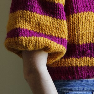 May include: A striped jumper with yellow and pink horizontal stripes. The jumper has a cropped length and a relaxed fit.