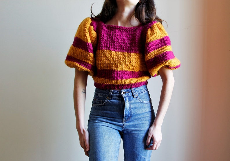 May include: A striped knit sweater with a cropped fit and puffed sleeves. The sweater is yellow and pink.