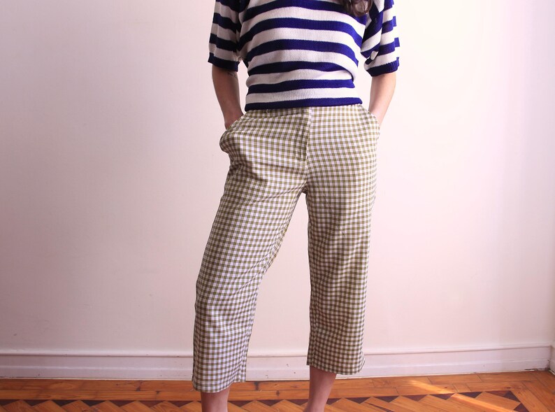 Pu&ograve; includere: Una persona indossa una maglietta a maniche corte a righe blu e bianche e pantaloni cropped a quadri verde oliva e bianchi. I pantaloni hanno tasche e sono al ginocchio. L'outfit &egrave; casual ed elegante.