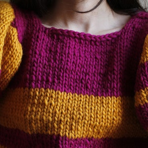 May include: A striped knitted jumper with yellow and purple stripes. The jumper has a round neckline and long sleeves.