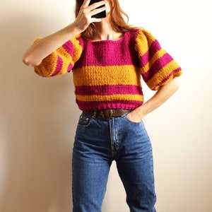 May include: A striped jumper with yellow and pink horizontal stripes. The jumper has puffed sleeves and a square neckline.