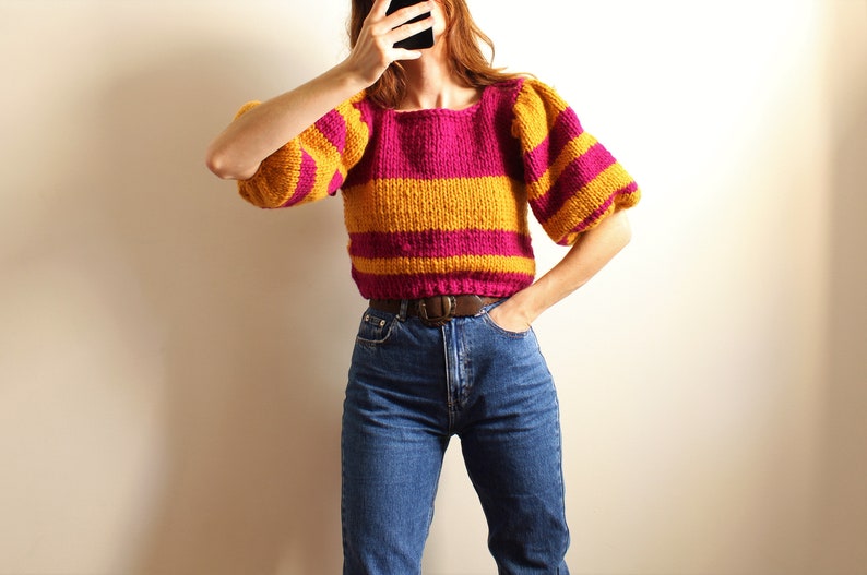 May include: A striped jumper with yellow and pink horizontal stripes. The jumper has puffed sleeves and a square neckline.