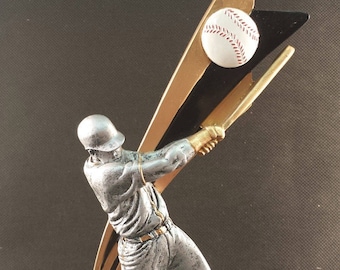 May include: A silver baseball trophy featuring a batter mid-swing, poised to hit a baseball. The baseball is white with red stitching. The trophy has gold and black accents and sits on a gray base.