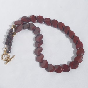 May include: A red gemstone necklace with a gold clasp. The necklace is made of small, round beads and larger, leaf-shaped beads.
