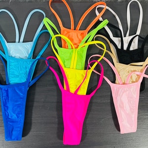 Puede incluir: Una colección de braguitas de bikini tipo tanga de colores brillantes, incluyendo azul, naranja, verde, amarillo, rosa, negro, blanco y beige. La ropa de baño presenta tirantes finos y un diseño minimalista, adecuada para la playa o la piscina.