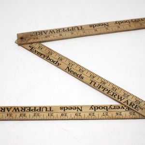May include: A wooden folding ruler with the text "Everybody Needs TUPPERWARE" printed on both sides. The ruler is marked in inches.