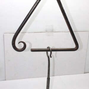 May include: A dark metal triangle musical instrument with a curved end and a striker. The triangle is suspended by a white string. The striker is a metal rod with a hook.