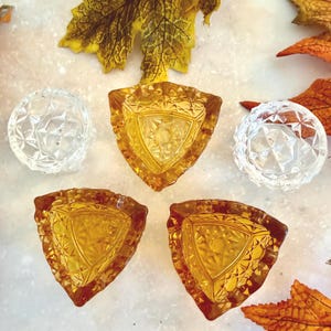 May include: A collection of five glass dishes featuring three amber-colored triangular pieces with a geometric pressed pattern and two clear circular pieces with a faceted diamond-like texture, arranged together on a light surface.