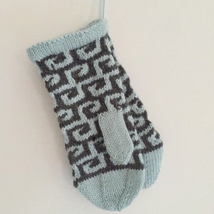 May include: A pair of light blue knitted mittens with a geometric pattern in dark grey. The mittens have a thumb hole and a loop at the top for hanging.