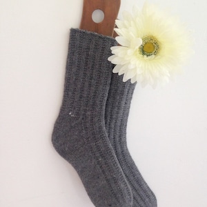 Pode incluir: Um par de meias de lã cinzas penduradas em um cabide de madeira com uma flor branca.