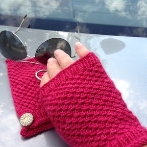 May include: A pair of pink knitted fingerless gloves with a button detail. The gloves are made with a textured stitch pattern.