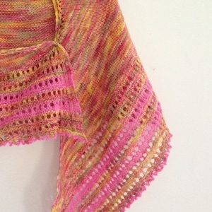 Puede incluir: Un chal de punto rosa y amarillo con un borde de encaje. El chal está hecho con un hilo jaspeado que crea un efecto a rayas.