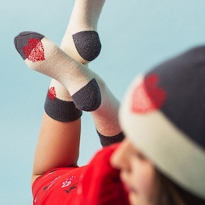 May include: A person wearing a red floral dress and a white and navy blue beanie with red hearts. The person is also wearing white socks with navy blue and red heart accents.