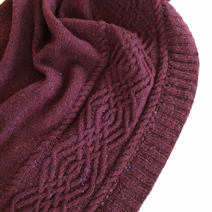 May include: A close-up of a burgundy knitted sweater with a cable knit pattern on the edge. The sweater is folded and the texture of the knit is visible.