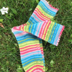 May include: A pair of colorful striped socks with a pink, green, blue, and yellow color scheme. The socks are knitted with a lacy pattern and have a scalloped edge.