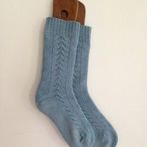 May include: A pair of light blue knitted socks with a delicate lace pattern. The socks are hanging on a wooden hanger.