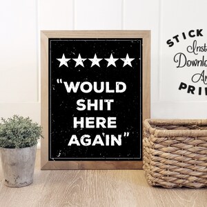 Puede incluir: Una impresión enmarcada con fondo negro y texto blanco que dice "Would Shit Here Again" con cinco estrellas sobre el texto. La impresión está en un marco de madera y está sobre un suelo de madera.