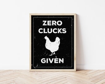 Puede incluir: Arte de pared enmarcado con fondo negro y texto blanco, y una silueta de pollo. El texto dice "ZERO CLUCKS GIVEN". El marco es de color marrón claro y se muestra sobre un suelo de madera clara.