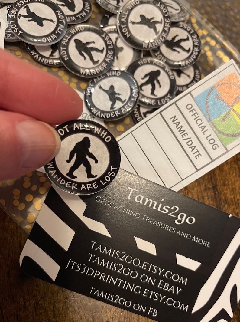 May include: A selection of black and white Bigfoot-themed badges, each with the phrase "Not All Who Wander Are Lost." The badges feature a Bigfoot silhouette and are likely for geocaching.