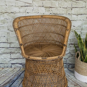 May include: A woven wicker chair with a rounded back and a wide, circular base. The chair is made of natural brown wicker and has a woven pattern.