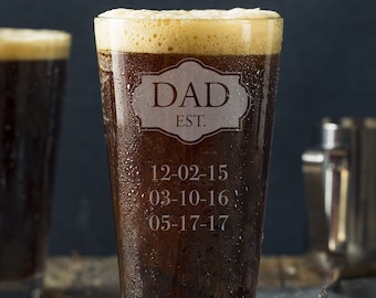 Könnte beinhalten: Ein klares Glas Pint-Glas mit einer braunen Flüssigkeit darin. Das Glas ist mit den Worten "DAD EST." und den Daten "12-02-15", "03-10-16" und "05-17-17" graviert.