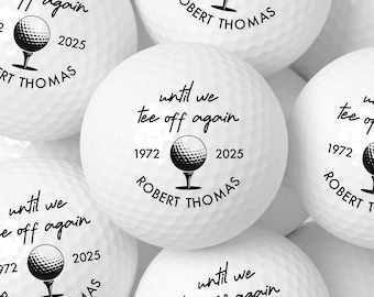 May include: White golf balls with black text and graphics. Each ball features the phrase "until we tee off again", the years 1972 and 2025, and the name "ROBERT THOMAS". The golf balls have a dimpled surface.