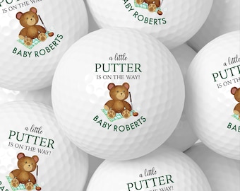Può includere: Palline da golf bianche con un orsacchiotto, una mazza da golf e il testo "a little PUTTER IS ON THE WAY!" e "BABY ROBERTS". Le palline da golf hanno un tema baby shower o gender reveal.