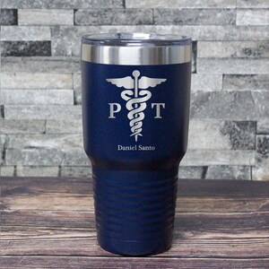May include: A navy blue stainless steel tumbler with a silver caduceus symbol and the letters "PT" on either side of the symbol. The name "Daniel Santo" is engraved below the symbol.