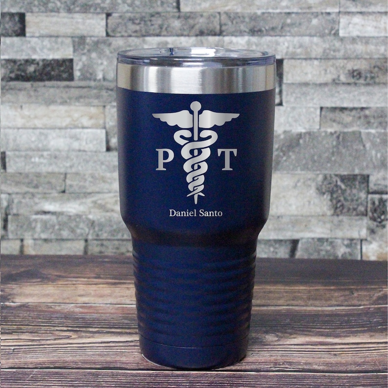 May include: A navy blue stainless steel tumbler with a silver caduceus symbol and the letters "PT" on either side of the symbol. The name "Daniel Santo" is engraved below the symbol.