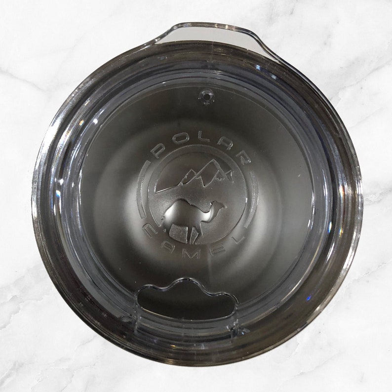 May include: Close-up of a stainless steel travel mug with a clear lid. The mug has a black logo that says "Polar Camel" with a camel silhouette and mountain range graphic.