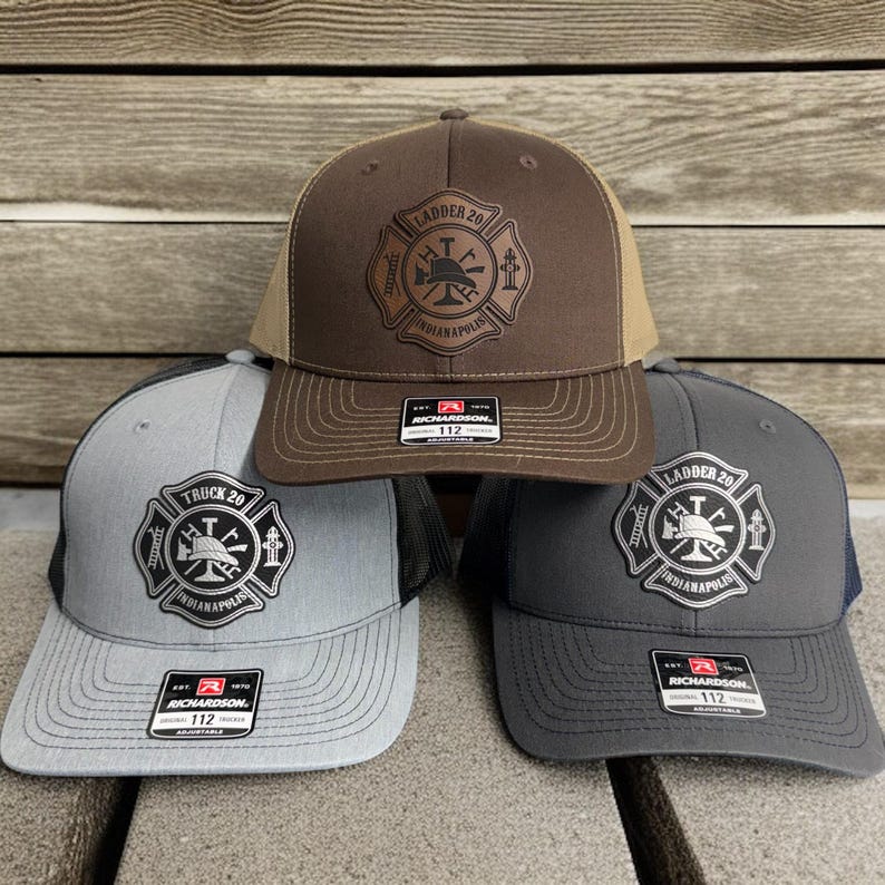 May include: Three adjustable trucker hats featuring a leather-like patch with a firefighter emblem. The top hat is brown, the bottom left is light gray, and the bottom right is dark gray. Each hat has a Richardson 112 label on the brim.