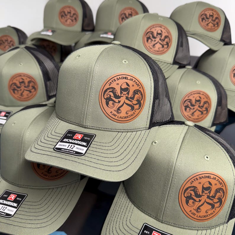 May include: A collection of olive green and black mesh trucker hats featuring a circular tan leather patch on the front. The patch displays an octopus graphic with the text JAYS BACHELOR PARTY 2023 FORT LAUDERDALE. Each hat has a Richardson 112 label.