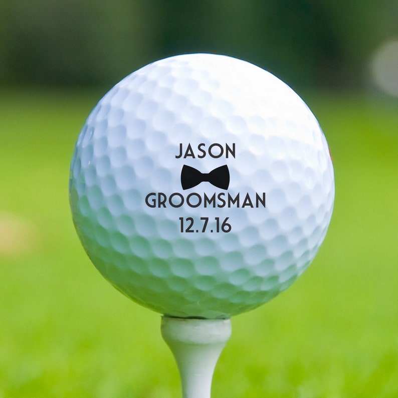 May include: White golf ball with black text and a bow tie graphic. The text reads "Jason Groomsman 12.7.16".
