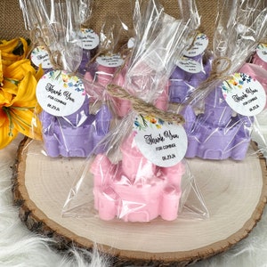May include: Purple and pink castle-shaped soap favors wrapped in clear cellophane bags with a floral thank you tag. The tag says "Thank You for Coming 06.29.24".