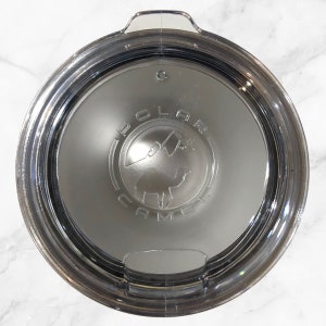 May include: A clear plastic lid with a silver rim and a black and white logo that says "Polar Camel" with a camel silhouette inside the logo.