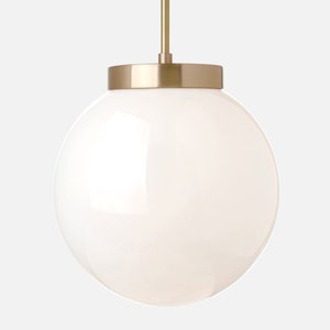 Op de afbeelding: Een moderne hanglamp met een grote, bolvormige witte glazen kap. Het heeft een goudkleurige metalen kap en een bijpassende ophangstang. Het ontwerp is eenvoudig en elegant, geschikt voor diverse interieurstijlen. De diameter is ongeveer 25 cm.