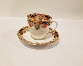 May include: A vintage teacup and saucer set with a floral pattern in shades of blue, green, orange, and gold. The cup and saucer have a white background with a gold rim.
